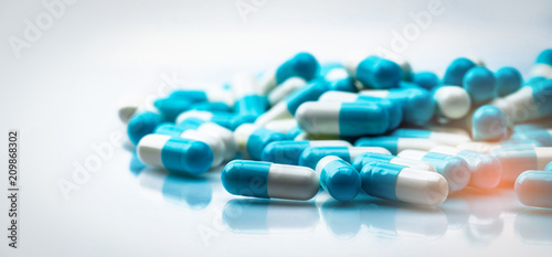 Selective focus on blue and white capsules pill spread on white background with shadow. Global healthcare concept. Antibiotics drug resistance. Antimicrobial capsule pills. Pharmaceutical industry.