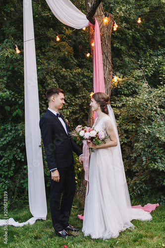 Evening summer rustic outdoor wedding ceremony. The bride and groom holding hands and see each other. photo