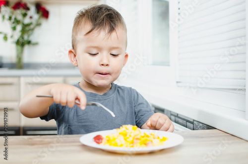 a child in a t-shirt in the kitchen eating an omelet, a fork