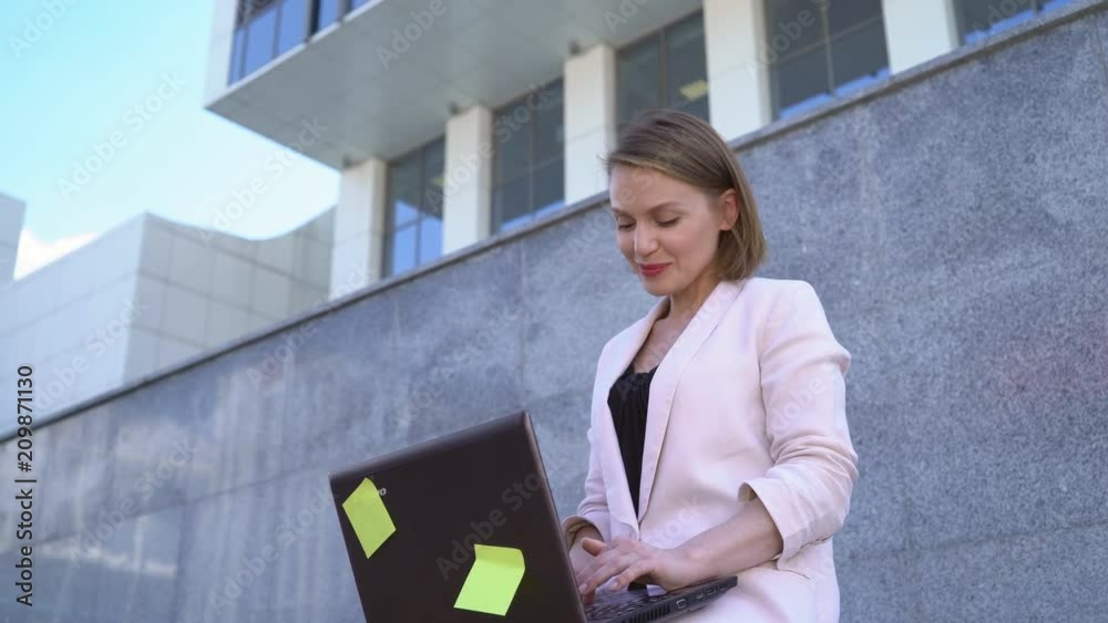 A female businesswoman working on a laptop outdoors. on the background of an office building. Attractive middle-aged woman in a jacket. 4K