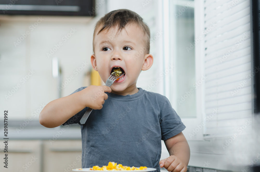 a child in a t-shirt in the kitchen eating an omelet, a fork a child in a t-shirt in the kitchen eating an omelet, a fork