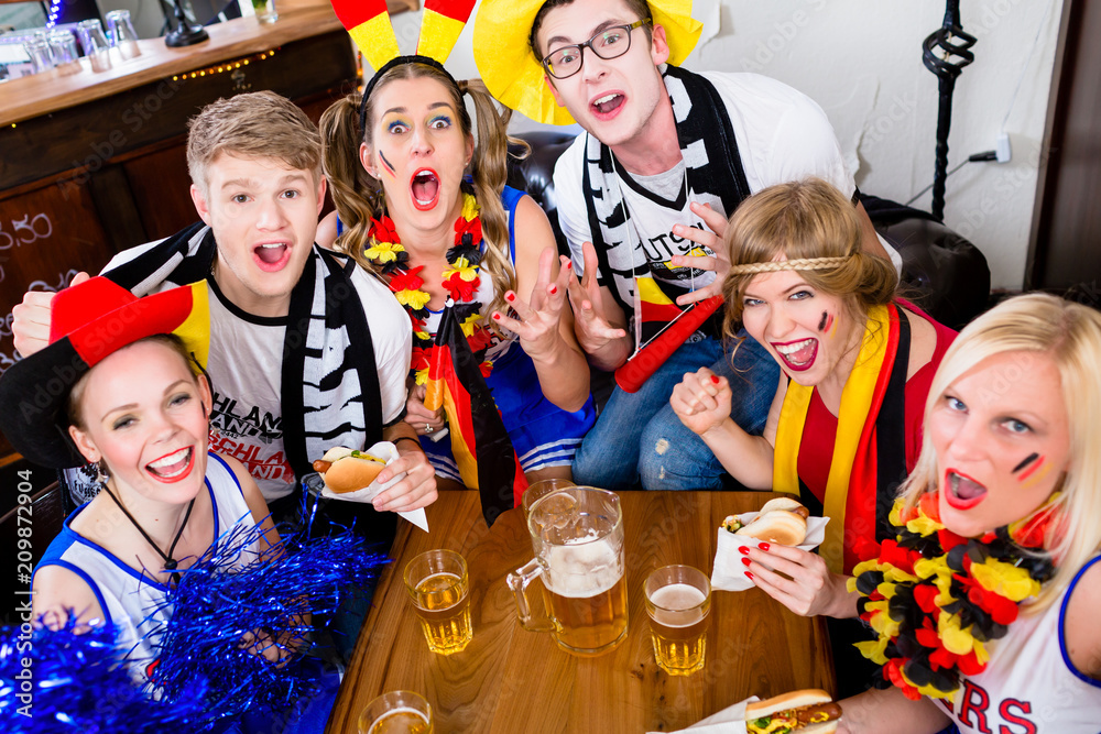 Fototapeta premium Football fans in sports bar watching a game with excitement wearing flags and make-up