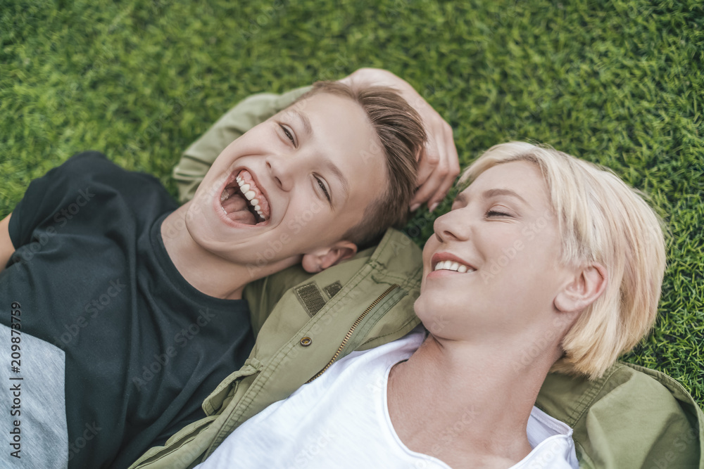 high angle view of happy mother and son laughing while lying together on grass high angle view of happy mother and son laughing while lying together on grass