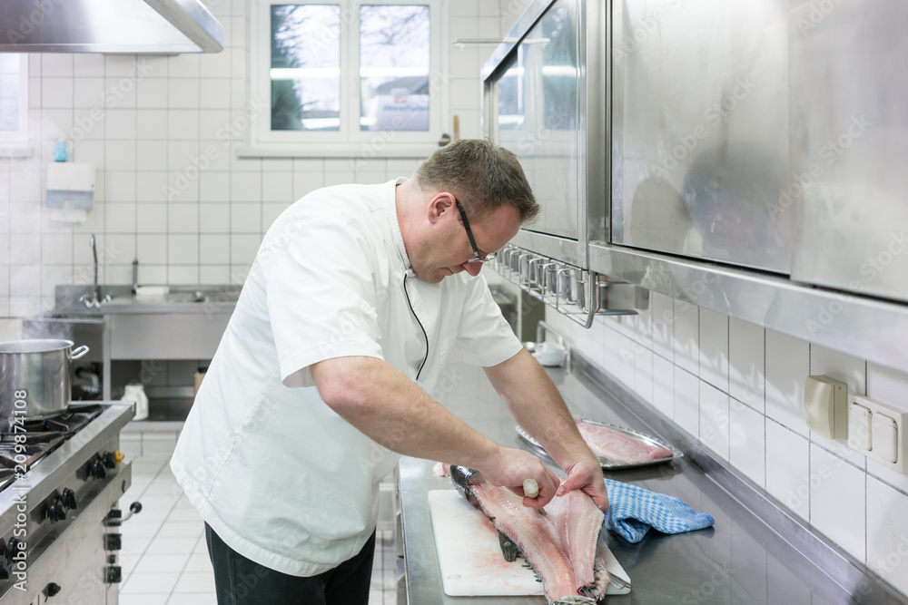 Chef in restaurant or hotel kitchen filleting carp fish Chef in restaurant or hotel kitchen filleting carp fish