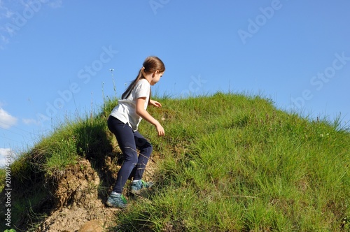 Child, blonde girl with long hair, climbing a little hill with green grass