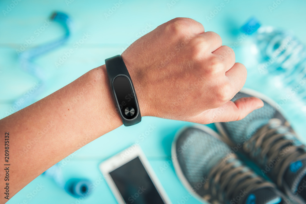 Fitness tracker on hand. Sneakers, bottle of water, tape measure on blue wooden background. Healthy lifestyle.