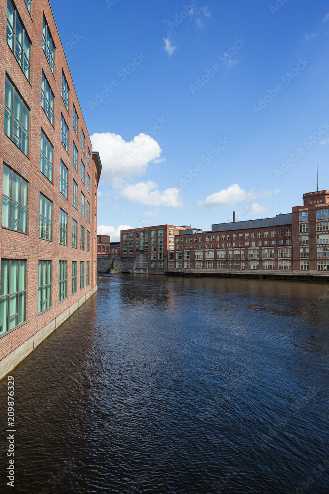 Old red brick industrial buildings along the Tammerkoski rapids in downtown Tampere, Finland on a sunny day.