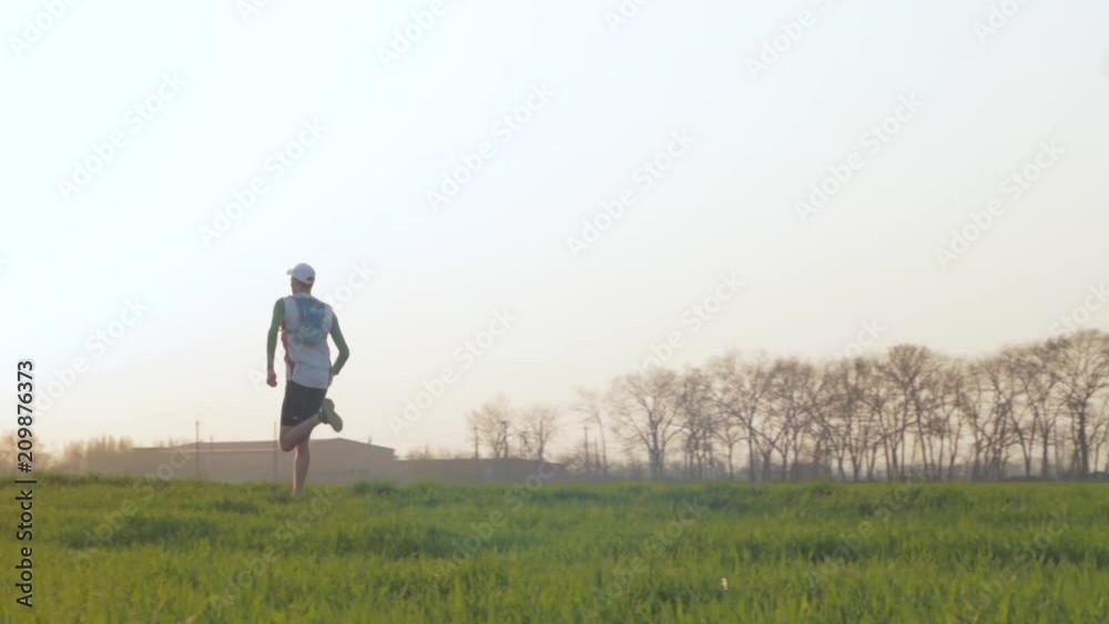 young male runner training outdoors in spring fields during beautiful sunset young male runner training outdoors in spring fields during beautiful sunset