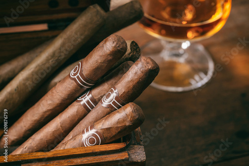Photo Cuban cigars closeup on wooden desk, blur glass of brandy