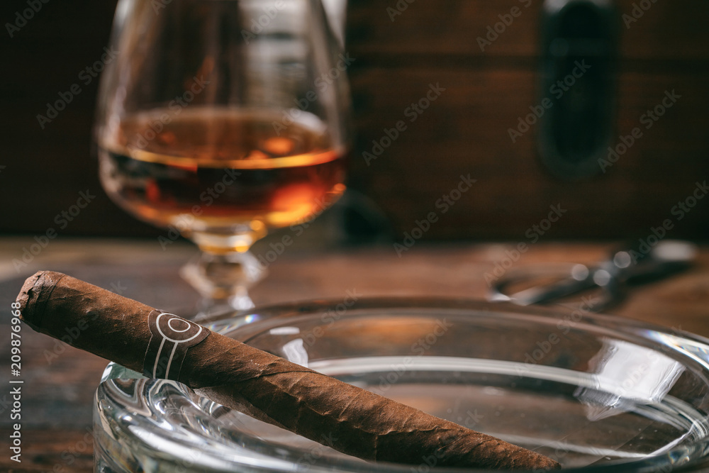 Cuban cigar in an ashtray, a glass of brandy, wooden background, copy space
