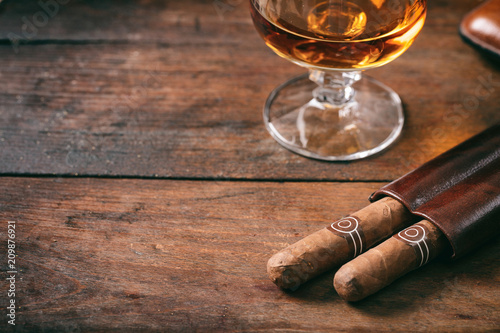 Cuban cigars closeup on wooden desk, blur glass of brandy photo