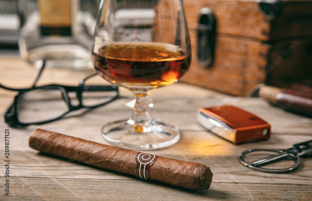 Cuban cigar closeup on wooden desk, blur glass of brandy