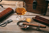 Cuban cigar and a glass of cognac brandy on wooden background