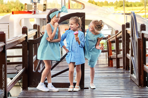 Group 3 fashion lady kids in elegant striped dresses in marine style.Little girls cool,summer clothes outdoors.Designer children's collection.Friendship,smile,resting together,standing on bridge.