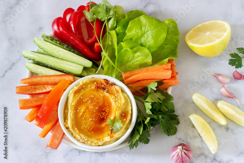Hummus, different vegetables and lettuce leaves with lemon and garlic on a light background. Vegan food.