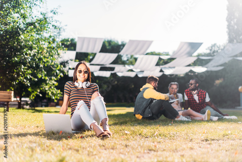 selective focus of young asian woman with laptop and multiracial friends behind resting on green grass in park © LIGHTFIELD STUDIOS