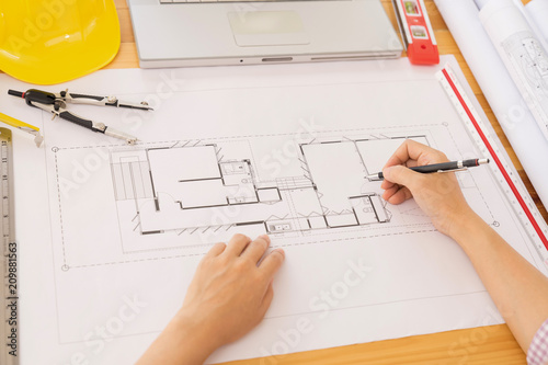 Top view, Architect or engineer hands working on blueprint plans  with a pencil ,laptopa ruler, calculator,  and engineering tools. Architect or engineer working on blueprint in office.  photo