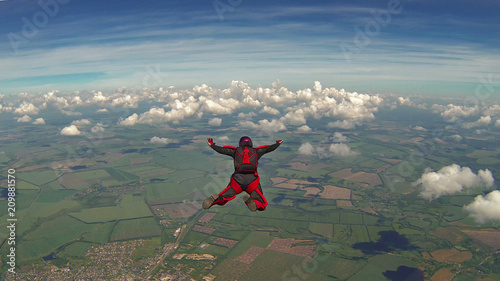 Obraz na plátně Skydiver in a red jumpsuit freefalling above the clouds