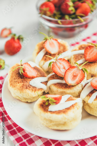 Homemade cottage cheese pancakes with sour cream and fresh strawberry on white wooden background. Healthy breakfast.