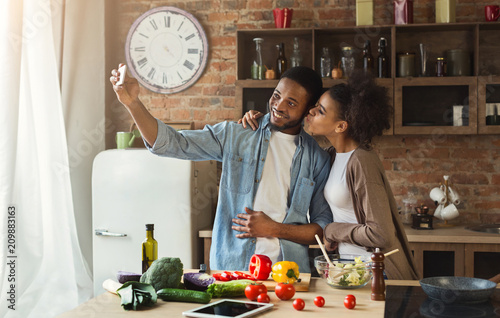 Happy african-american couple taking selfie with smartphone at kitchen photo