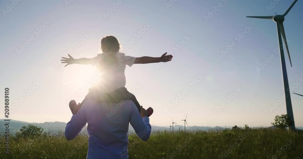 A father engineer holds his daughter in his arms and runs between the wind turbines with great freedom. Concept of: environmental engineering, renewable energy and love for nature and for the family