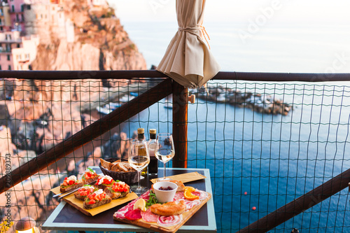 Romantic dinner for two at sunset. White wine and Tasty italian snack: fresh bruschettes  and meat on the board in outdoor cafe with amazing view in Manarola