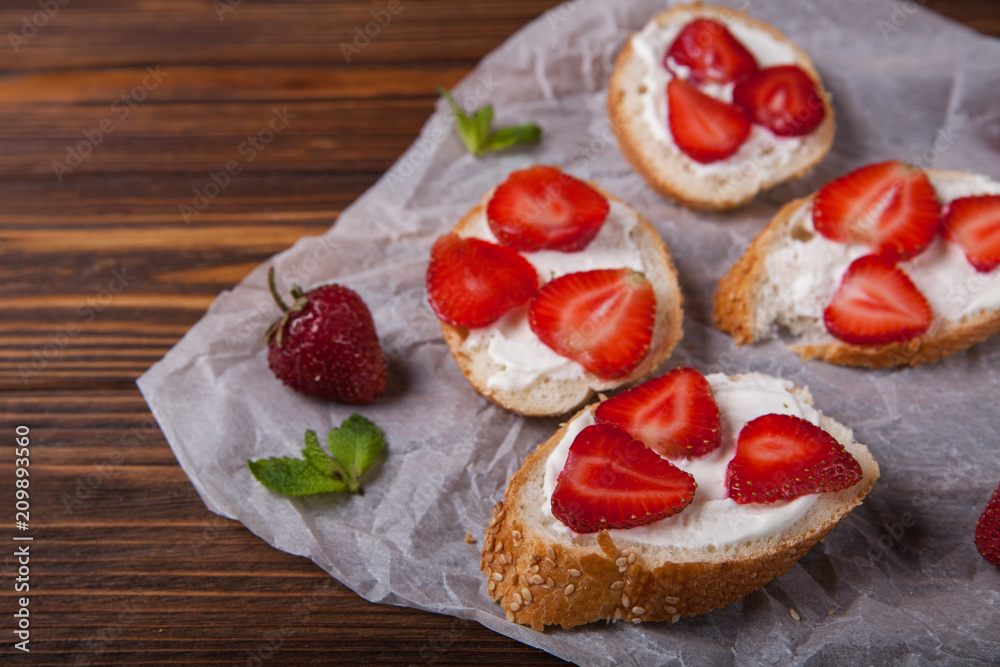Toasts or bruschetta with strawberries on cream cheese on wooden background. Top view. Copy space Toasts or bruschetta with strawberries on cream cheese on wooden background. Top view. Copy space