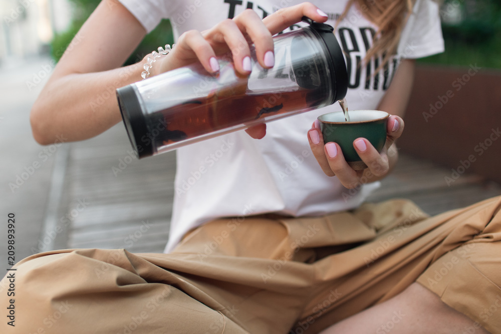 Traveler girl pouring tea in thermos cup, outdoors. Young woman drinking tea at cup. Theme travel. Woman pouring a hot drink in mug. Traveler girl pouring tea in thermos cup, outdoors. Young woman drinking tea at cup. Theme travel. Woman pouring a hot drink in mug.