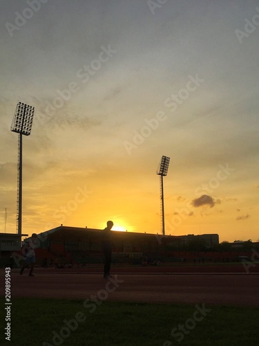 Silhouette and shadow of people running and jogging in the stadium and lane with the spot lighe pole and light of sunset in background. photo