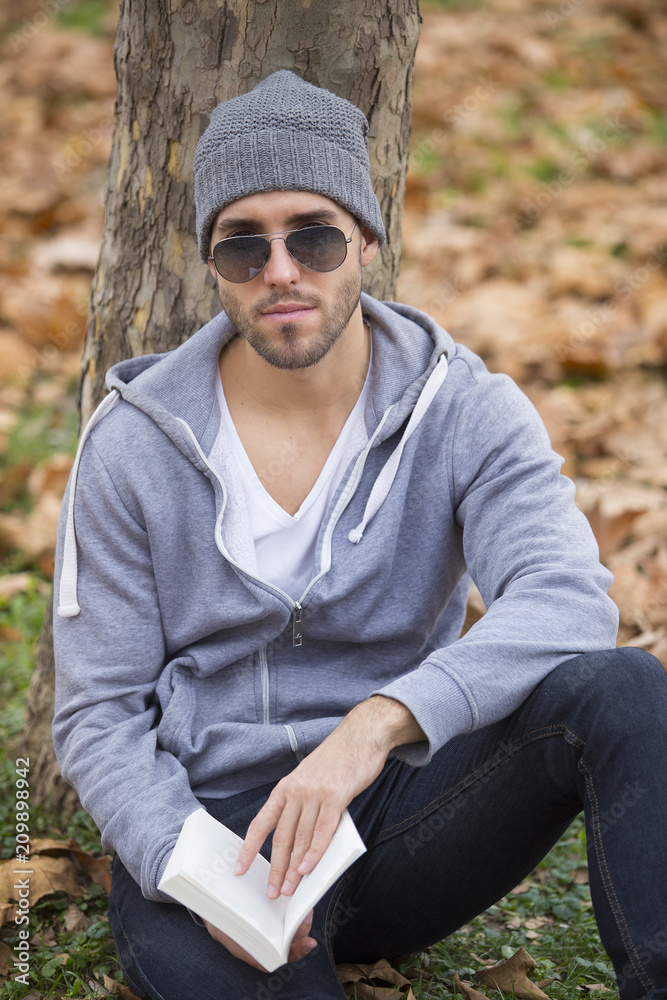 Fototapeta premium Handsome man in nature reading a book. Autumn leaves. Copy space