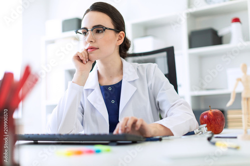 A beautiful young girl in a white robe is sitting at the table and typing on the keyboard. photo