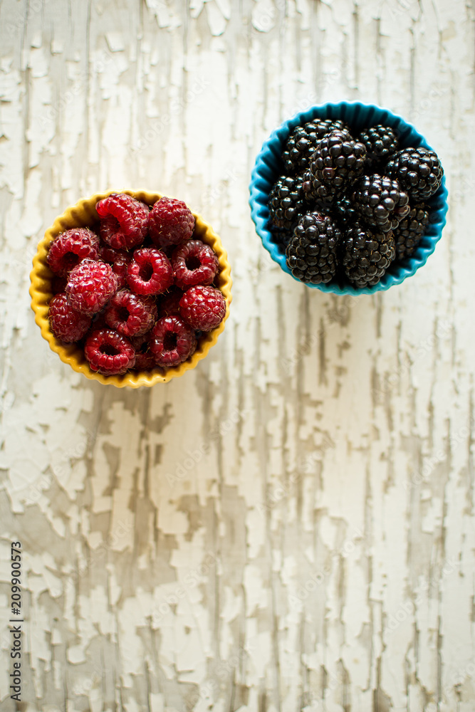 Raspberries and Blackberries in Ceramic Bowls on Rustic Background