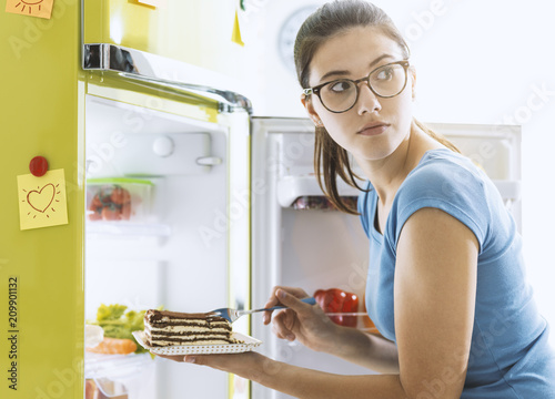 Obraz na plátně Hungry woman taking a dessert from the fridge