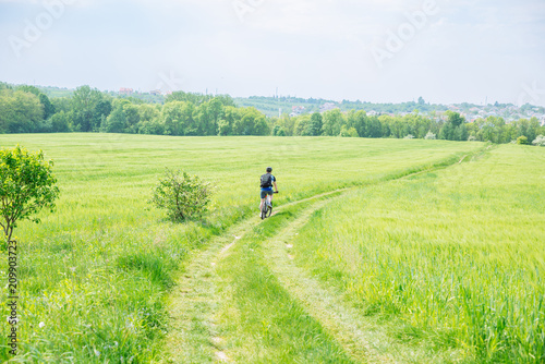 man riding bicycle by trail in green barley field. copy space © phpetrunina14