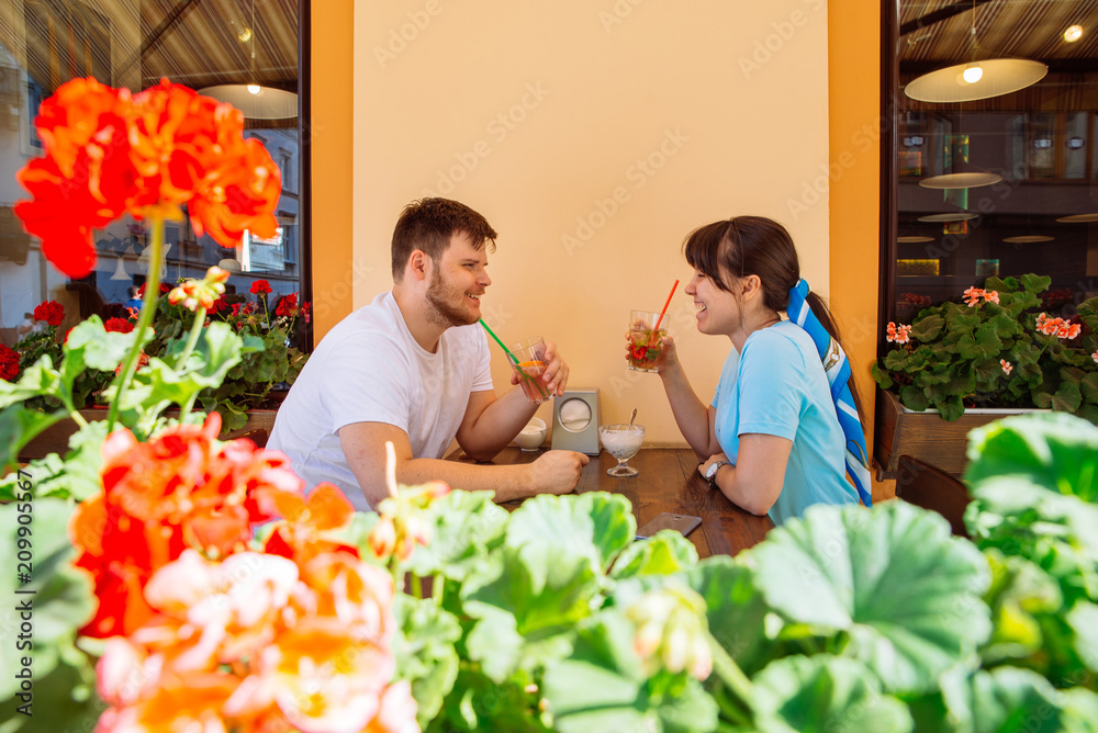 Naklejka premium couple sitting in summer cafe drinking cool drinks and talking