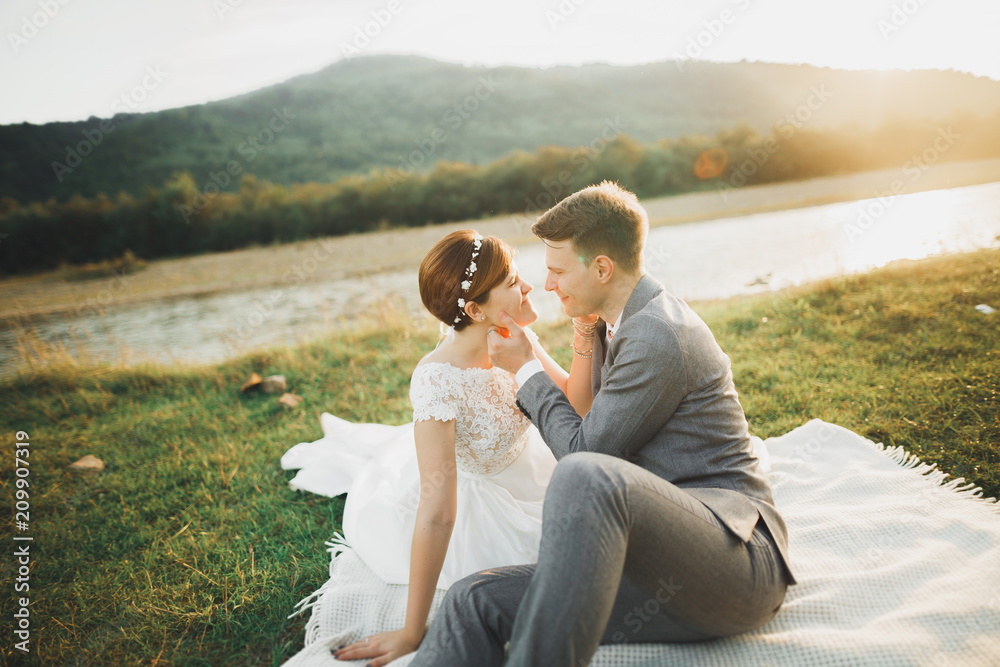 Young newly wed couple, bride and groom kissing, hugging on perfect view of mountains, blue sky Young newly wed couple, bride and groom kissing, hugging on perfect view of mountains, blue sky
