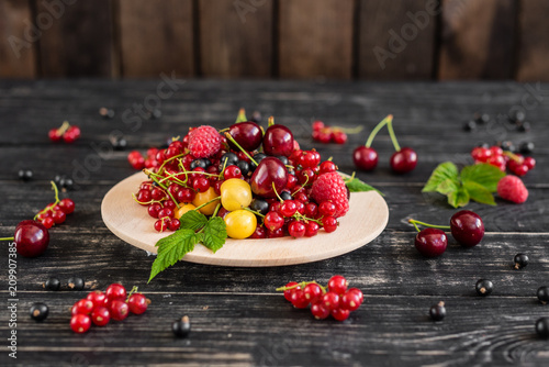 Raspberry, cherry, red currant, blackcurrant on a wooden plate against a dark background. It can be used as a background