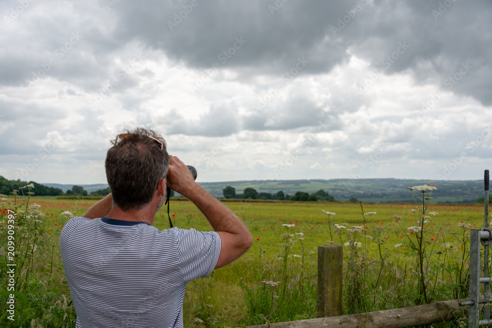 man in striped T shirt with beard looking at distant scenery with binoculars man in striped T shirt with beard looking at distant scenery with binoculars