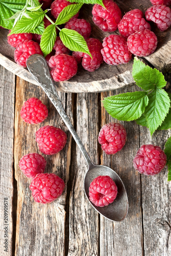 Fresh raspberries with leaves on rustic wooden background, top view