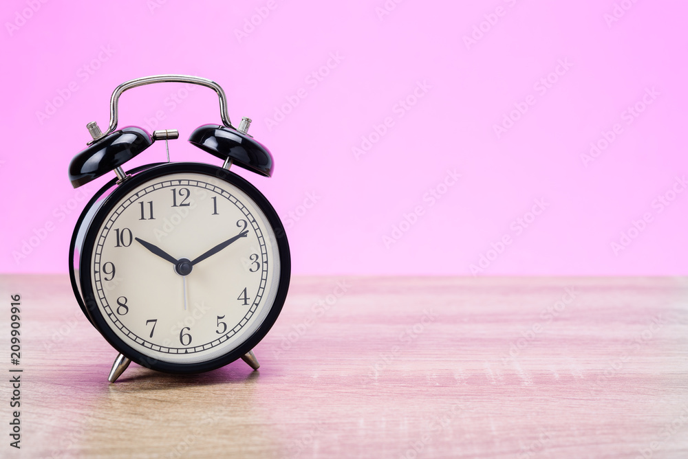 Black retro Alarm clock on wooden table with pink background. Black retro Alarm clock on wooden table with pink background.