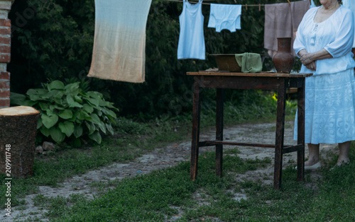an old woman in white stands near a table on which lie prinadzheshnosti for washing. Hanging clothes and linen, it dries. yard