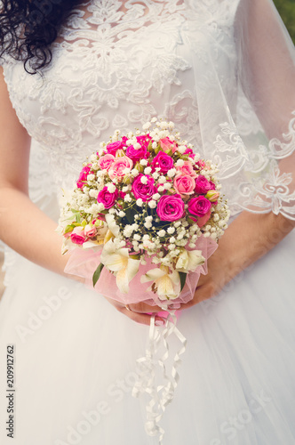 A bride in a white wedding dress is holding a bouquet in her hands. Close-up, selective focus. Toning in the style of instagram.