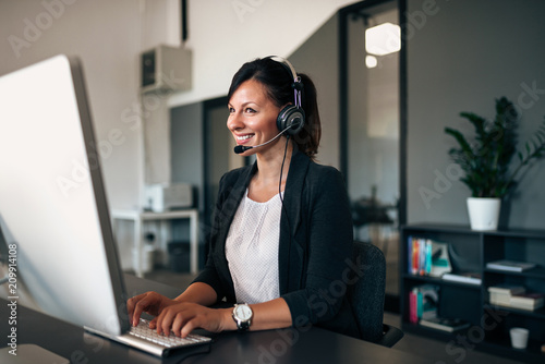 Beautiful customer representative with headset smiling during conversation with a client. photo