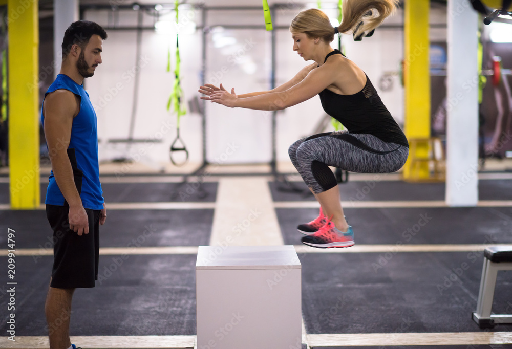 woman working out with personal trainer jumping on fit box woman working out with personal trainer jumping on fit box
