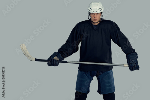 Canvas Print Hockey player wearing black protective gear and white helmet holds a hockey stick on a gray background