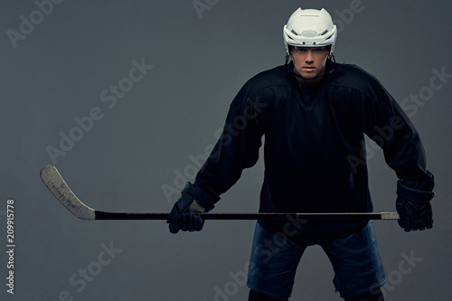 Canvas Print Hockey player wearing black protective gear and white helmet holds a hockey stick on a gray background