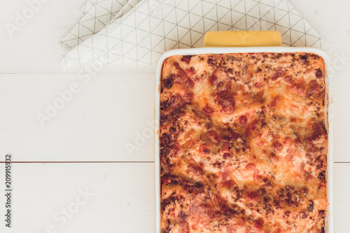Italian Lasagna Bolognese with Beef, Tomato Sauce and Green Basil on Rustic White Wooden Background