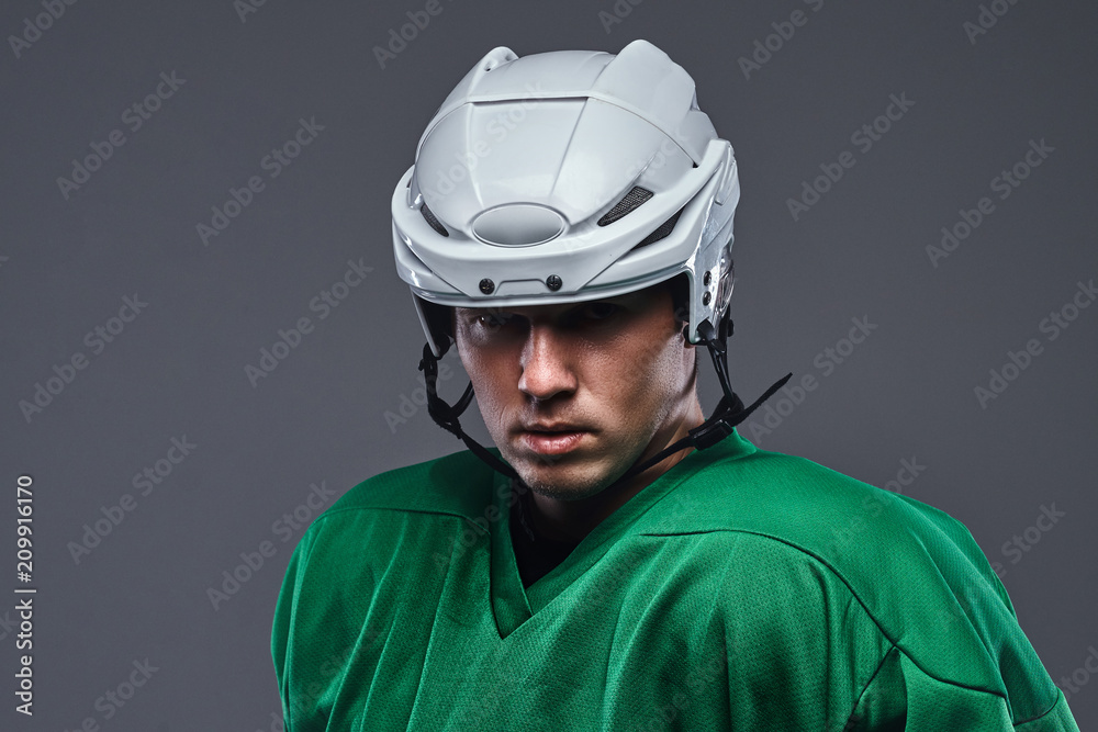 Naklejka premium Close-up portrait of a professional hockey player in a protective sportswear and helmet on a gray background.