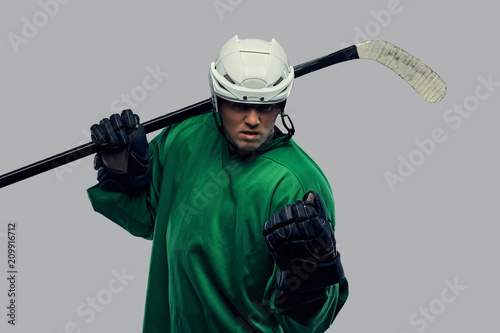 Canvas Print Angry professional hockey player in green sportswear standing with a hockey stick on a gray background