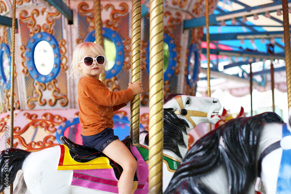 Cute Little Toddler Girl in Big Sunglasses Riding on Carnival Carousal